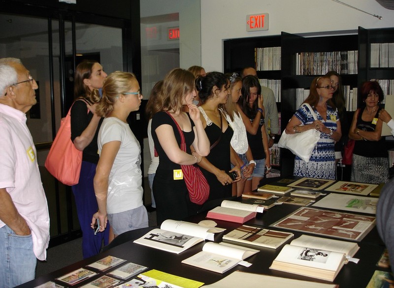 A group of people stand in front of a table covered in an array of open and closed books.