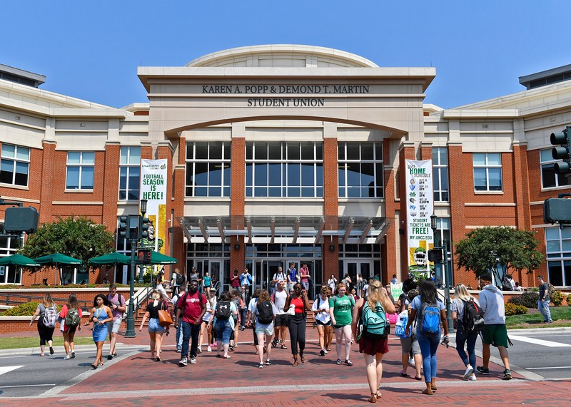 Many students walking to and from the Karen Popp & Demond Martin Student Union across the Craver Road crosswalk on a clear and sunny day.