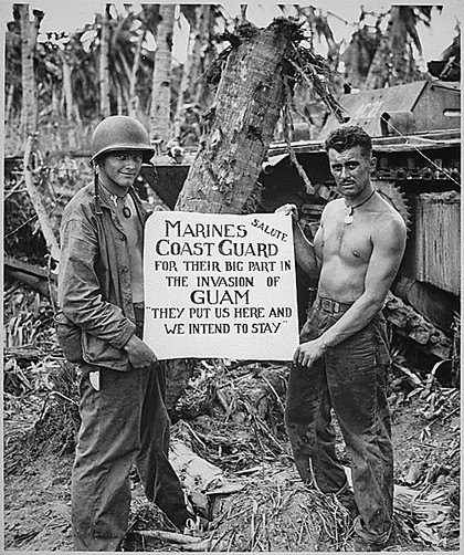 Appreciative U.S. Marines during the Pacific Campaign.
PFC Class William A. McCoy and PFC Ralph L. Plunkett hold a sign saluting Coast Guard forces after Japanese forces were defeated in Guam. U.S. Coast Guard photo.