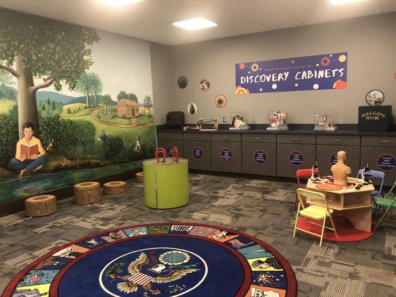 Interior of the Lincoln Learning Lab, with magnet table, a presidential rug, and discovery cabinets full of replicas.