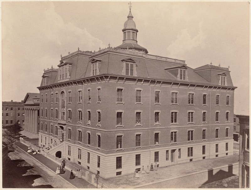 Black and White, sepia tones. Four story masonry building with a mansard roof and cupola.