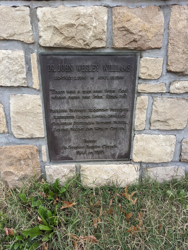 A close-up of a metal plaque set on the front of a stone brick surface. The plaque reads: DR. JOHN WESLEY WILLIAMS [new paragraph] JANUARY 2, 1906 to APRIL 22, 1988 [new paragraph] "There was a man sent from God whose name was John. " (John 1:6) [new paragraph] FEARLESS PROPHET, ELOQUENT PREACHER, RESPECTED LEADER, LOVING HUSBAND, CHRISTIAN STATESMAN, FAITHFUL PASTOR, LOVING PARENT AND WORLD CITIZEN [new paragraph] Pastor [new line] St. Stephen Baptist Church [new line]