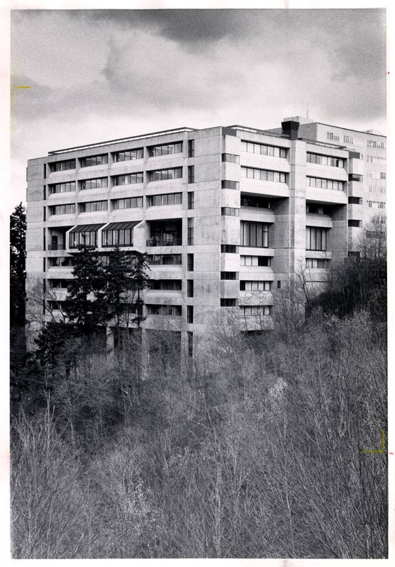 Large Brutalist building surrounded by trees and hills.