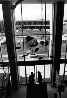 A view from the second floor of the library entry lobby, ca. 1969. In the foreground is a piece of art hanging from the ceiling, and in the background is the Liberal Arts building. The fountain pool is visible between the buildings.