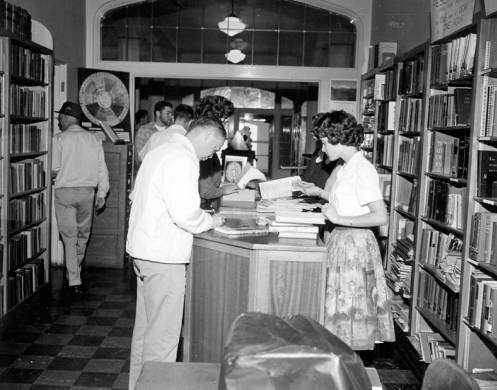 Students checking out books at the circulation desk in the library, when it was still located in the Administration building. The doors in the background are the first floor doors on the east end of the building, ca. 1960.