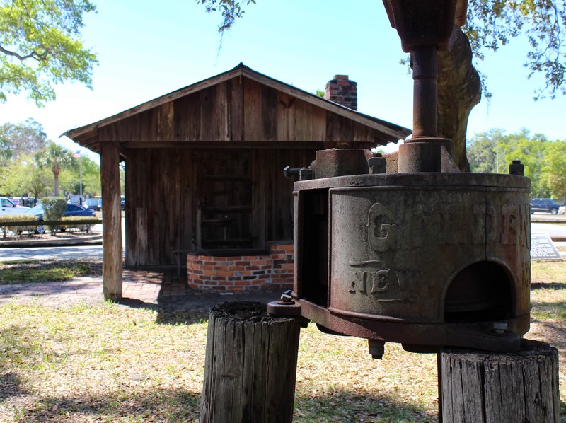 Sugarcane grinder with the smokehouse in the background by Lane Logan