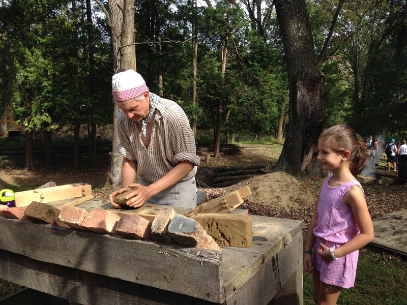 Image of a man in colonial clothing shaping clay into bricks