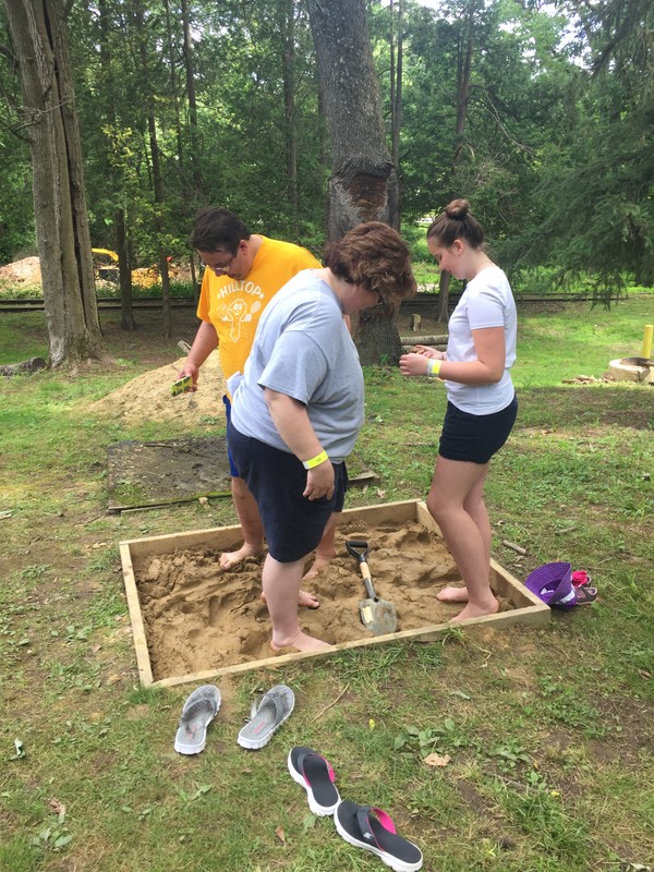 Image of three guests helping work the clay in a square pit