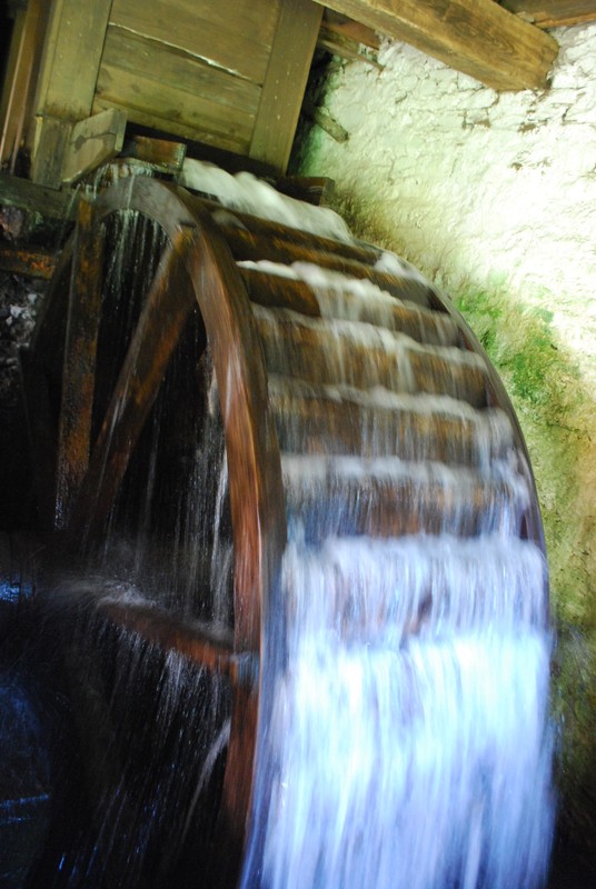 Image of wooden waterwheel with water rushing out over it.