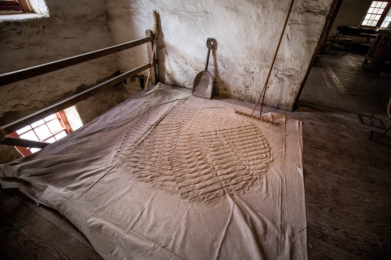 Image of flour spread out on the floor, with a wooden shovel and rake sitting nearby.