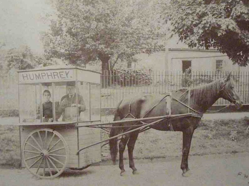 Photograph of a horse-drawn popcorn stand, with two men inside waiting for customers.