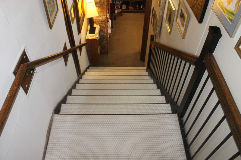 A flight of stairs, seen from the top of the stairs. They have black edging and the steps are covered with white hexagonal mosaic tile.