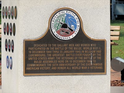 One side of the monument pedestal features a commemorative plaque, while the other sides have the insignias of participating divisions from the Battle of the Bulge. Image obtained from Waymarking.