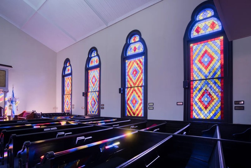 Three stained glass windows of blue, red, and yellow overlook the chamber of the synagogue.