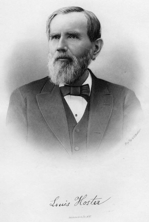 Louis Hoster sitting while wearing a suit with a black bowtie while sporting a beard.