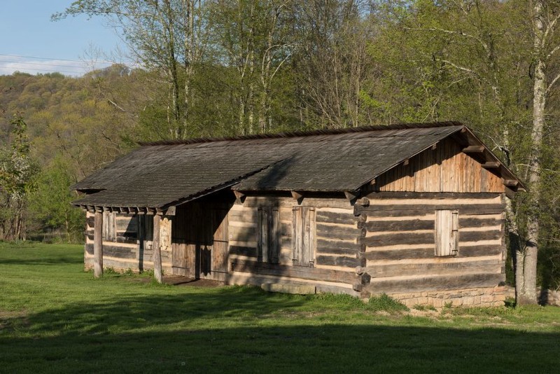 A log building with a large set of doors, several windows, and overhanging roof for visitors to observe blacksmithing demonstrations.
