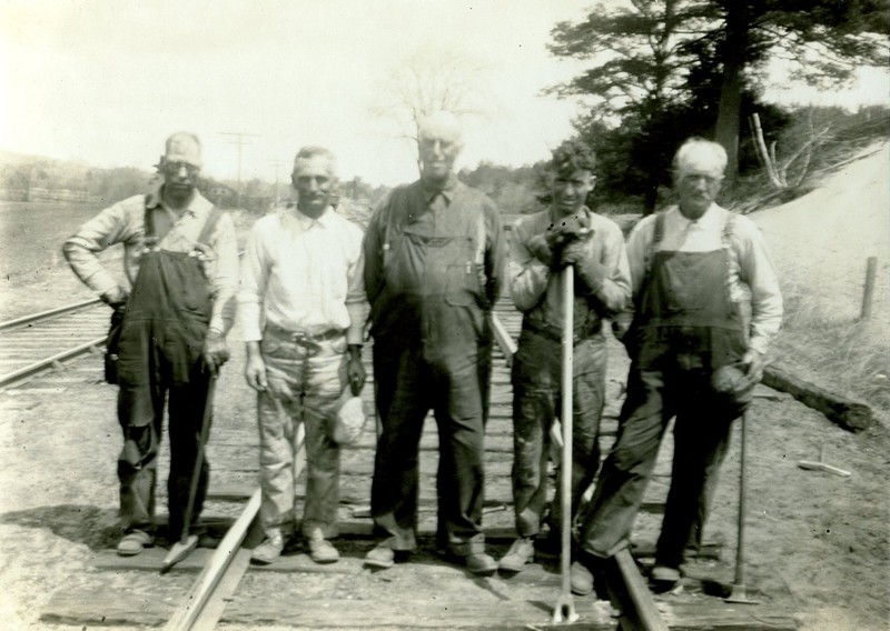 Section gang photo.  One of the two men in the center not holding any tools is likely the foreman.  The man on the left is holding a spike maul that is used to hammer spikes into the ties.  The man second from the right (Theodore Mack of Webster) is holding a spike puller,  a long tool with a forked end used for removing spikes.  