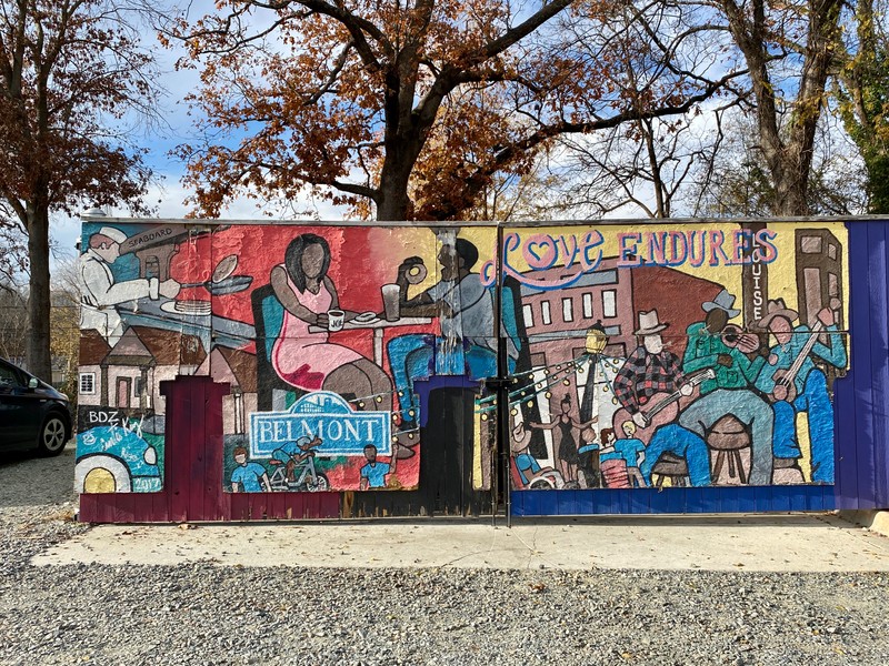 A variety of historic buildings and people in neighborhood settings are painted on a trash enclosure.