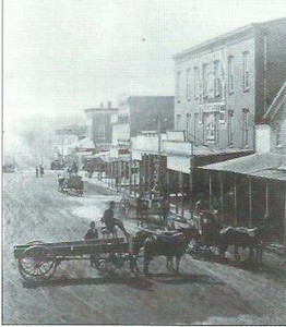 Regan Building is seen here as the original three story building surrounded by smaller frame buildings on the west side of the square, circa 1885.