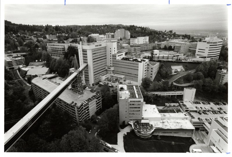 Black and white photograph of Marquam Hill Campus taken from near or above the Veterans Affairs Medical Center (VAMC), centered on the skybridge connecting VAMC and University Hospital South. Looking northwest.