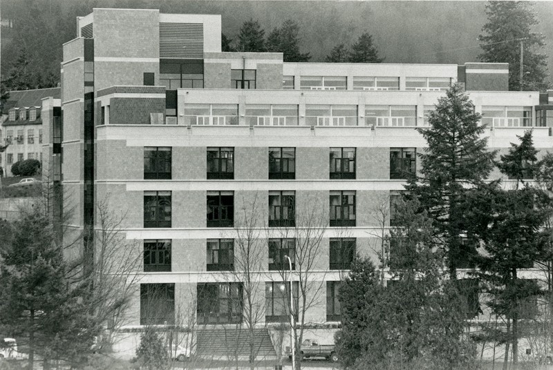 Black and white photograph of a large six-story brick building, modern style, surrounded by trees.