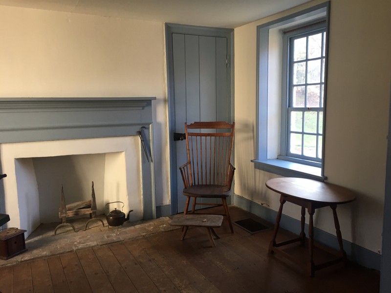 Image of a room with a fireplace, wooden armchair and wooden footstool, and a small table.