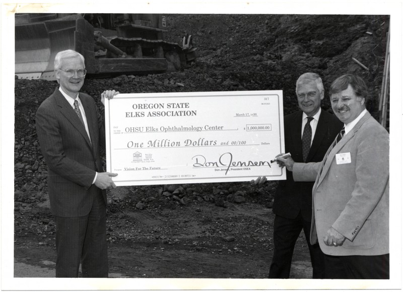 Black and white photograph of OHSU President Peter Kohler and Senator Mark O. Hatfield receiving a one million dollar check from the Oregon State Elks Association president Don Jensen for the Elks Childrens Eye Clinic at the Casey Eye Insitute at OHSU.