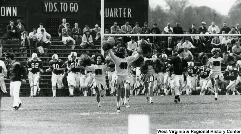 Mountaineer Cheerleaders bring the team onto the field, ca. 1968.