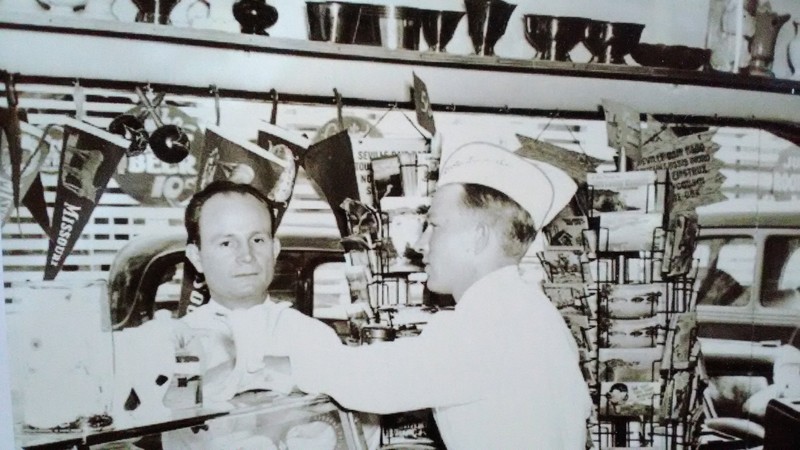 Bob Boots, right, and possibly Lee Crocker, left, at the counter of Boots Drive-In. Boots is standing in front of two postcard racks. Photograph courtesy the late Robert Boots, Powers Museum Collection.