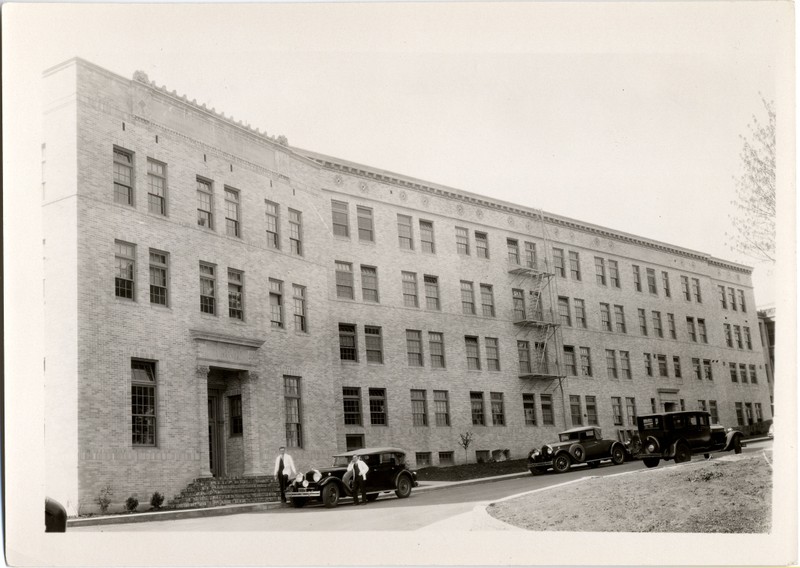 Black and white photograph of University of Oregon Medical School Outpatient Clinic and Doernbecher Memorial Hospital for Children with two doctors standing by an automobile near the outpatient entrance. 