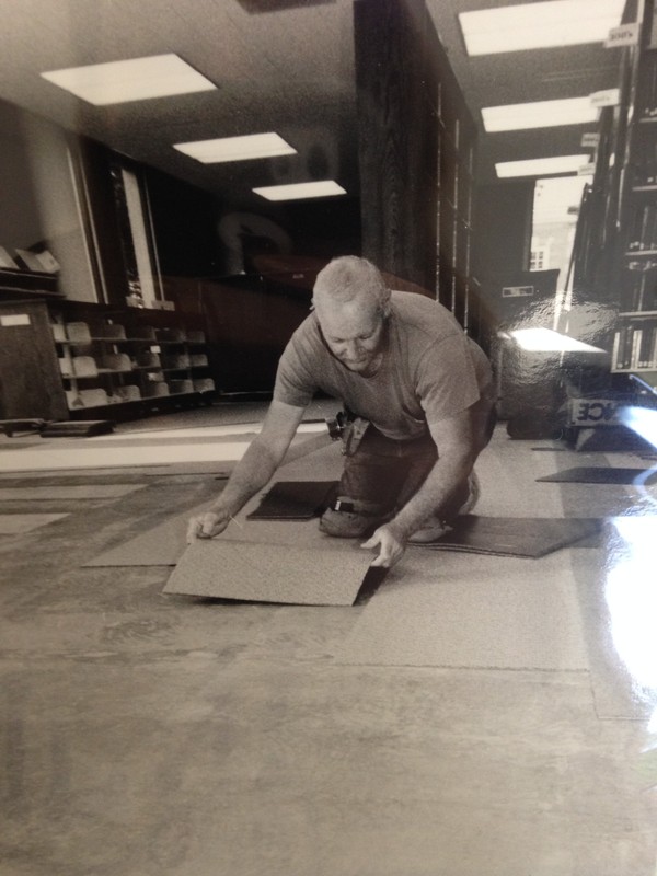 This is a photograph of a worker laying the carpet during the construction of Schewe Library.