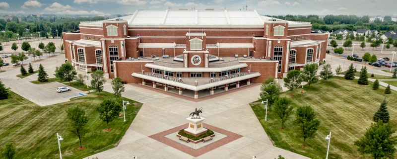 Aerial view of the grand main entrance to the arena. A bronze statue of Sitting Bull on horseback stands on a pillar in the middle of the entry plaza. 