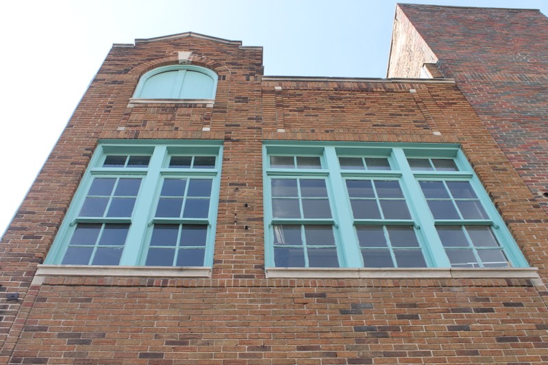 The rear of a three story building built with sand-colored brick, with window frames and hatches in cyan.