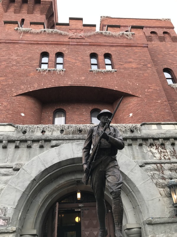 Another front shot of statue, with exterior of building behind the statue. The building behind is the original armory building which has been converted into a community space, museum and YMCA