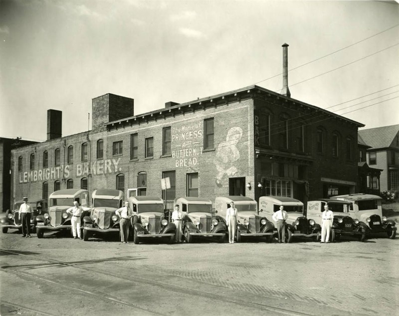 Lembright's Bakery located at 179 East Market Street with several deliverymen and delivery trucks. The sign on the side of the building reads, "Lembright's Bakery. The home of Princess and Butternut Bread."