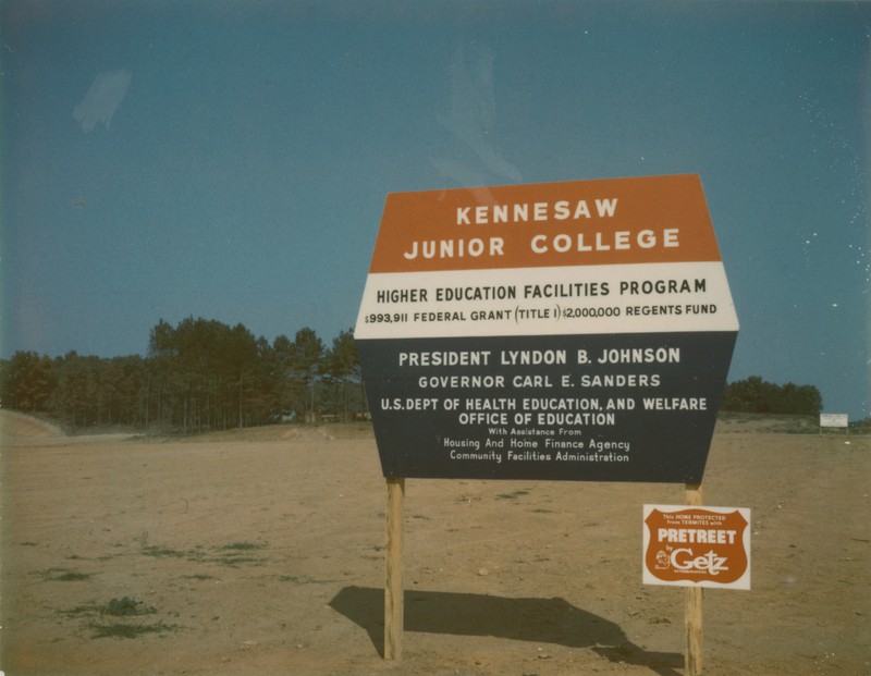 Red, white, and blue sign at the construction site for Kennesaw Junior College explaining that funding came through the Higher Education Facilities Program, including a Federal grant of $993,911 and 2 million dollars from the State Regents Fund.