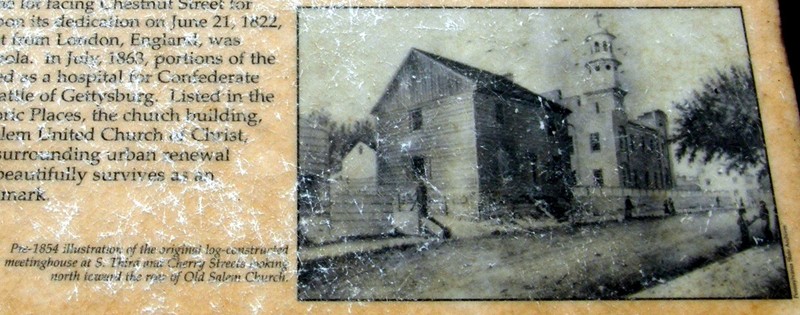 The log structure in the foreground is the Old Salem Church that was constructed in 1787. The tower of the new church can be seen in the background.