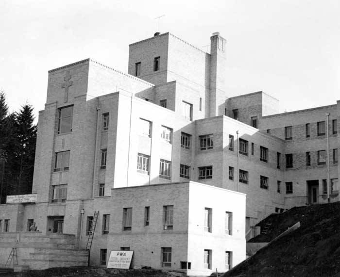 A large white building is viewed from the ground level. Construction signs are visible against the building.