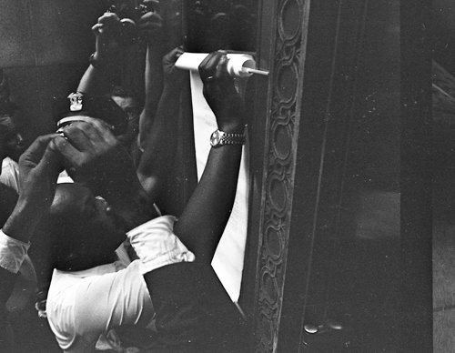 Echoing the 16th century protest of Martin Luther, King pins his demands to the door of City Hall. 