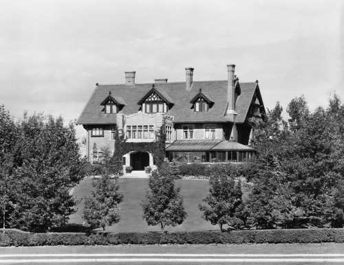 Black and white image of large and beautiful house with trees in foreground