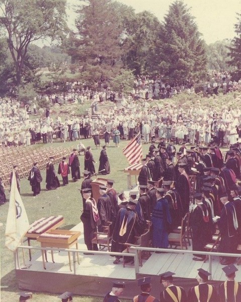 Ceremony on Metawampe lawn, ca. 1950. Faculty members in academic gowns walk past the podium during ceremonies on the lawn in front of the statue of Metawampe, a gift from the Class of 1950.