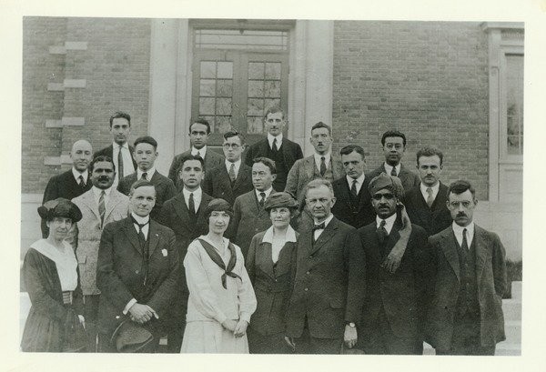 Kenyon L. Butterfield, 1922. Kenyon Butterfield is shown in the front row of a group of people who are posing on steps in front of a building. Written on the back of the photo: "College Cosmopolitan Club. 10 nationalities represented. About 1922". To