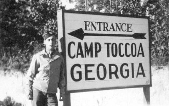 A soldier from the 506th Infantry Regiment standing at the entrance to Camp Toccoa while posing for a picture.