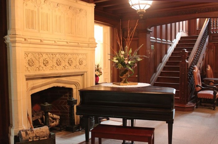 The mansion's large foyer with stone carved fireplace, piano and open staircase.