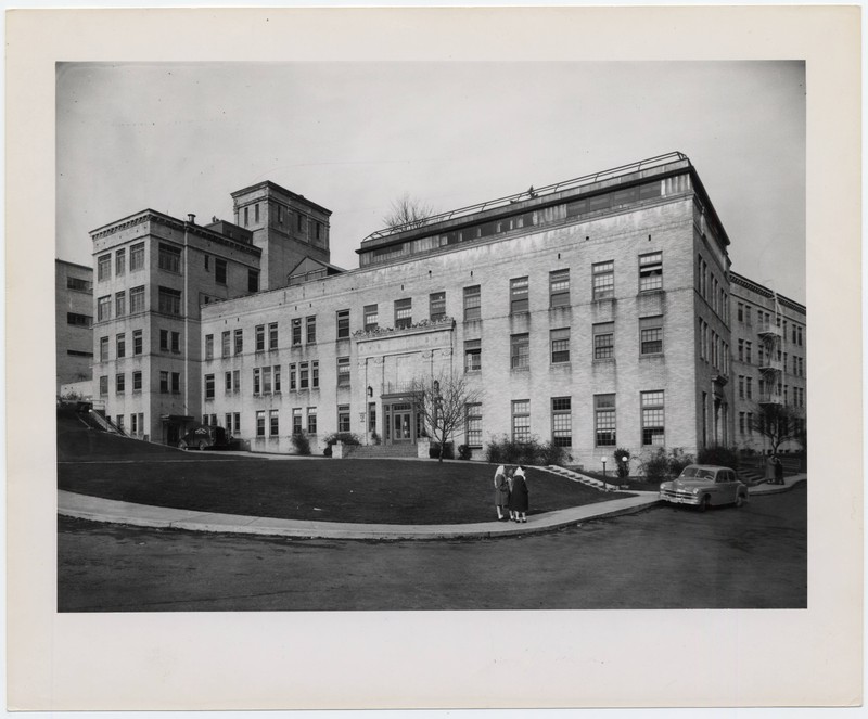 Black and white photograph showing the exterior and facade of the Doernbecher Memorial Hospital for Children, with two people in the foreground