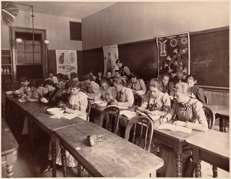 Black and White photo of young women in long-sleeved, long-dresses at classroom desks dissecting lobsters