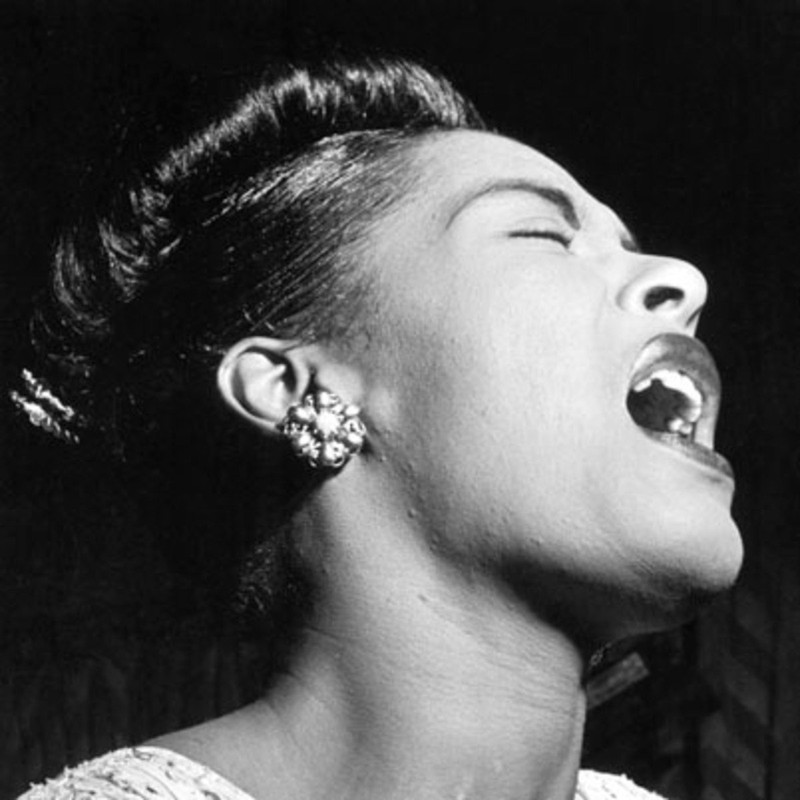 A photo of Billie Holiday performing. She was renowned for her ability to manipulate a microphone in order to be able to purr into it quietly or sing at very high volumes. Her style of working the microphone became the standard as others such as Frank Sin