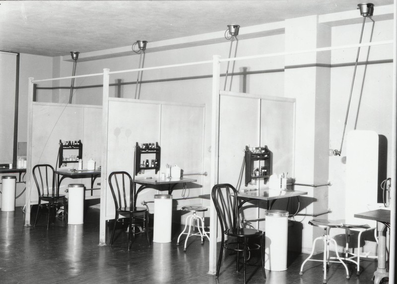 Black and white photograph of the Outpatient Clinic examination area at the University of Oregon Medical School. Four small examination areas with patient and provider chairs are separated by partial dividers. 