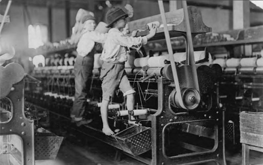 Two boys work to fix a broken bobbin by climbing onto the machine barefoot.