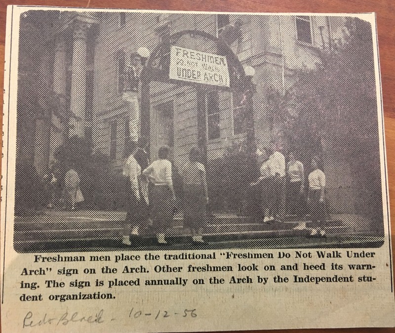 A historic photo from 1956 showing students placing a sign on the Arch warning freshmen to avoid walking under it
